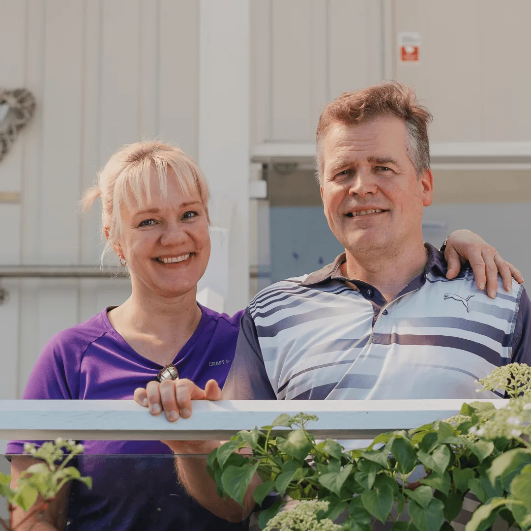 Hymyilevät asunnonomistajat seisovat ulkona ja katsovat valmista remonttikohdetta